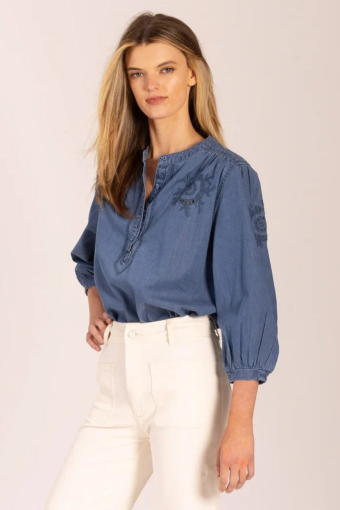 Woman wearing a blue blouse and white pants on a plain background