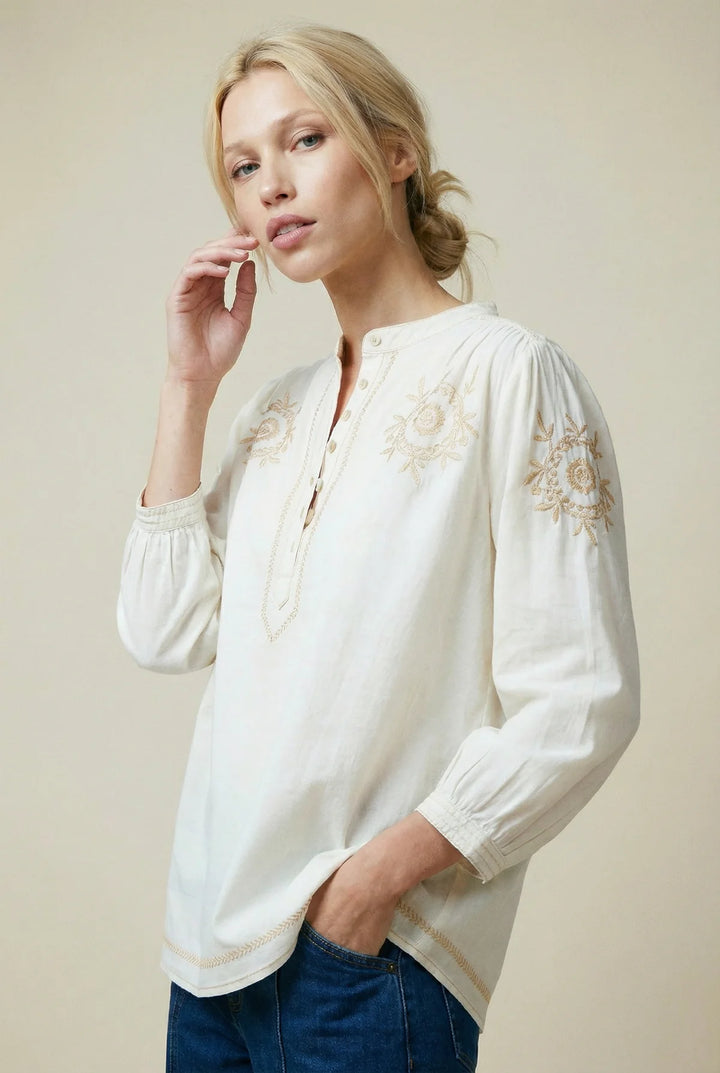 Woman wearing a white blouse with floral embroidery on a beige background