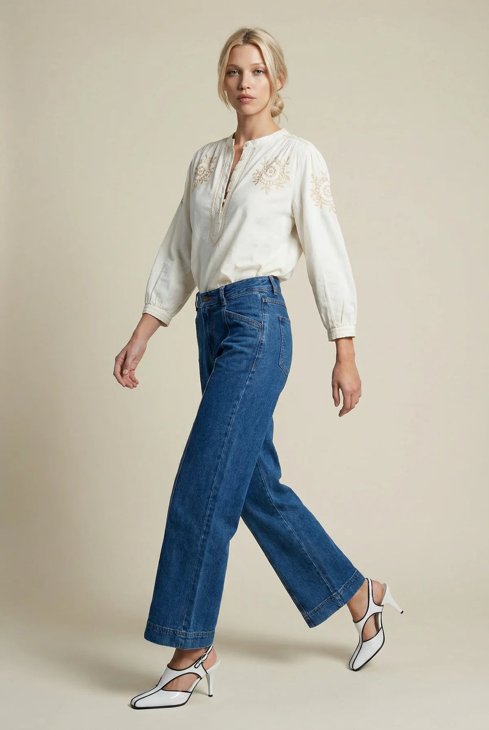 Woman wearing a white blouse with embroidery and blue jeans on a beige background