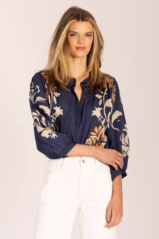 Woman wearing a navy floral blouse and white pants on a white background