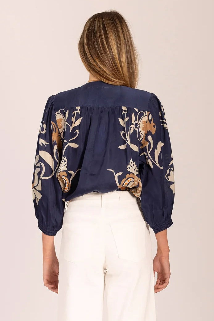 Person wearing a navy blue embroidered top and white pants on a plain background