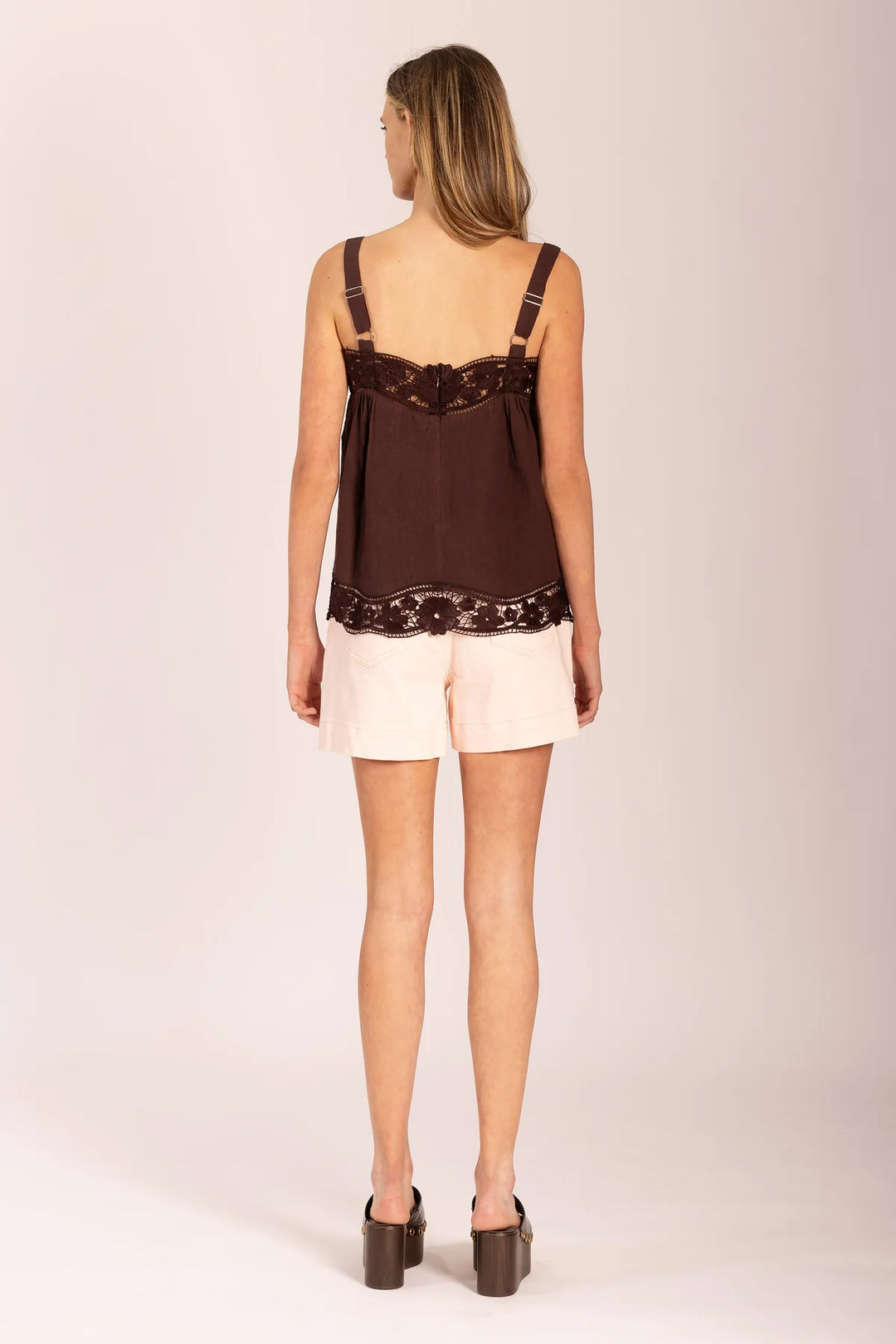 Woman wearing a brown top with lace details and beige shorts on a white background