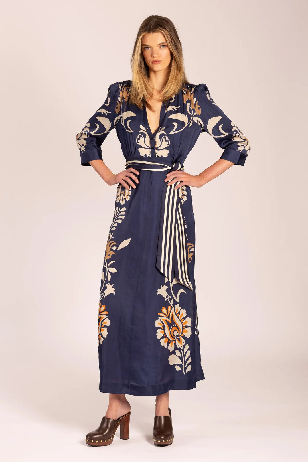 Woman wearing a long, dark blue dress with floral patterns on a white background