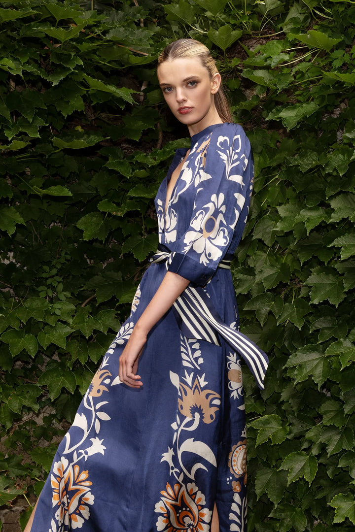 Woman wearing a blue floral dress standing against a green leafy background
