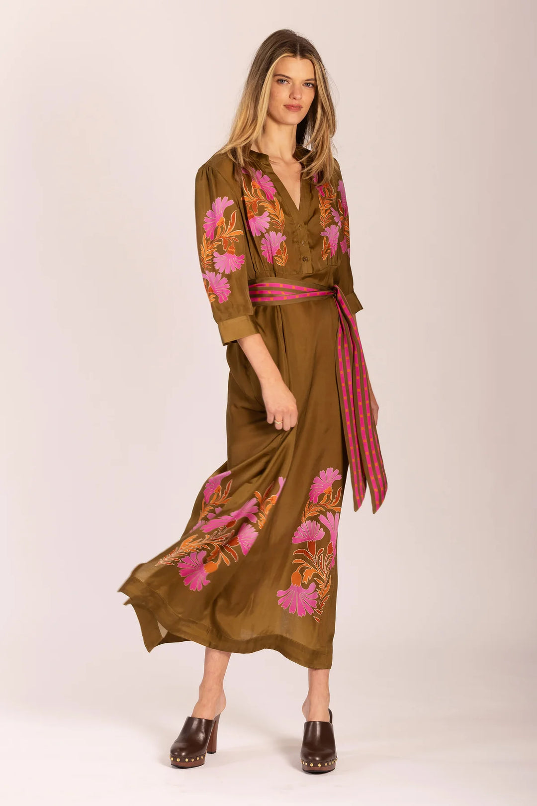 Woman wearing a brown dress with floral embroidery and a red belt on a white background