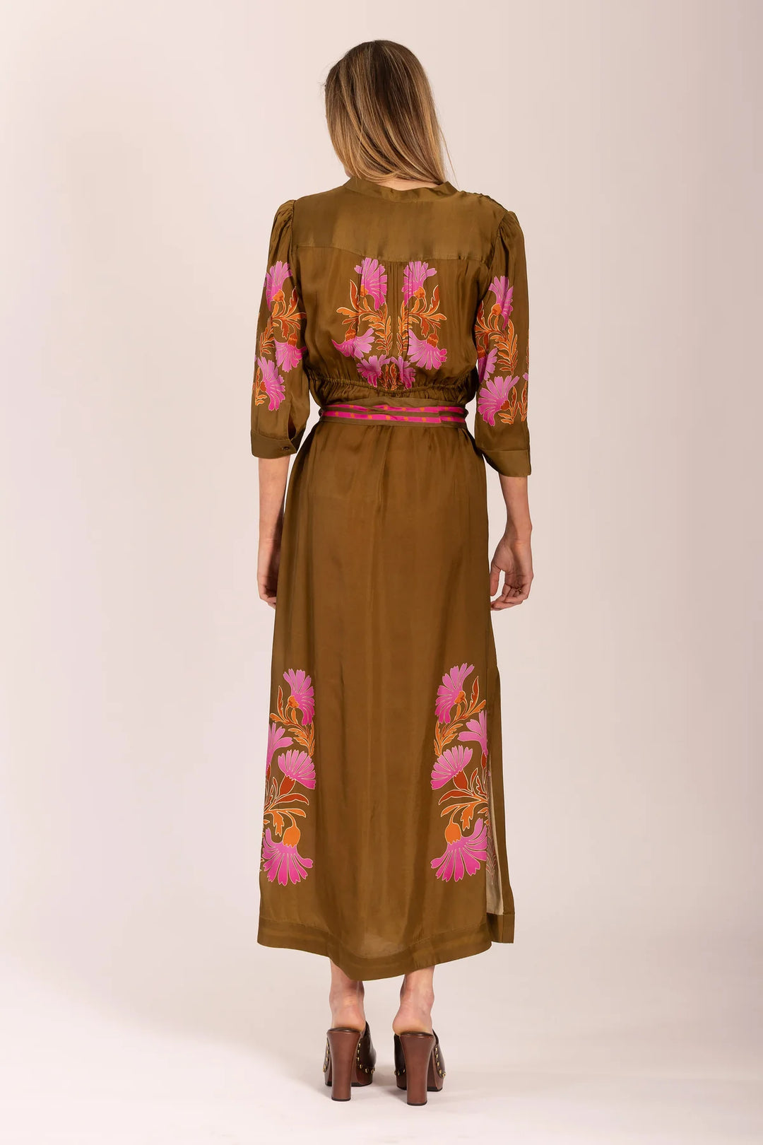 Woman wearing a brown dress with floral embroidery on a plain background