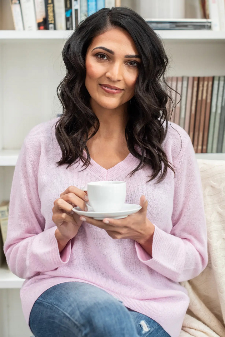 Woman holding a cup of coffee in a cozy room with books and plants.
