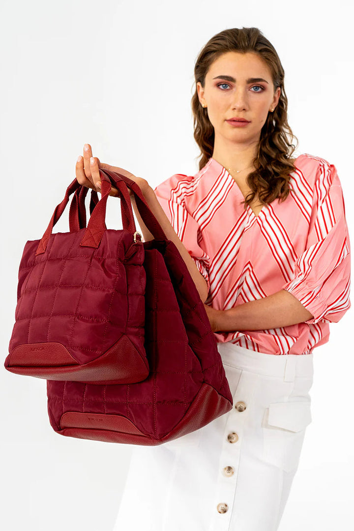 Woman holding two burgundy quilted handbags against a white background