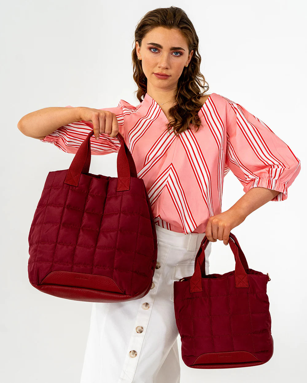 Woman holding two red handbags against a white background