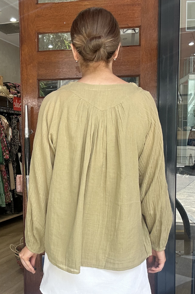 Person wearing a green blouse and white skirt in front of a store entrance.