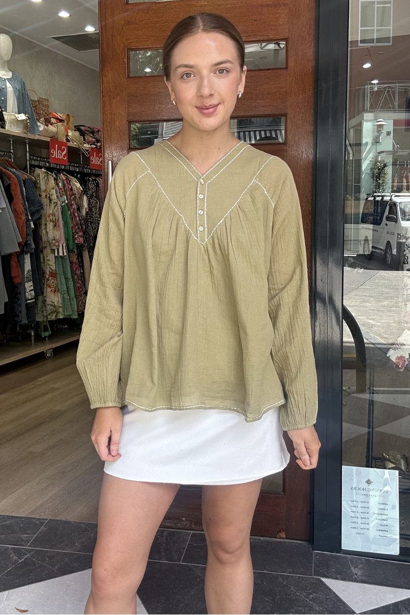 Woman wearing a green blouse and white skirt standing in front of a store entrance.
