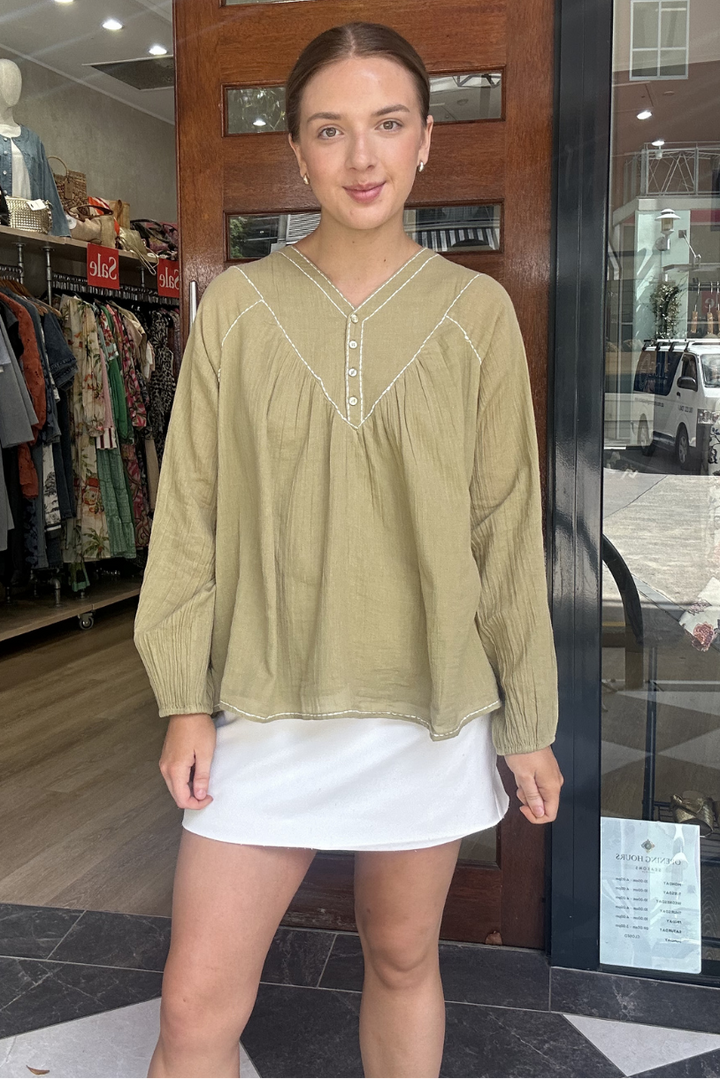Woman wearing a green blouse and white skirt standing in front of a store entrance.