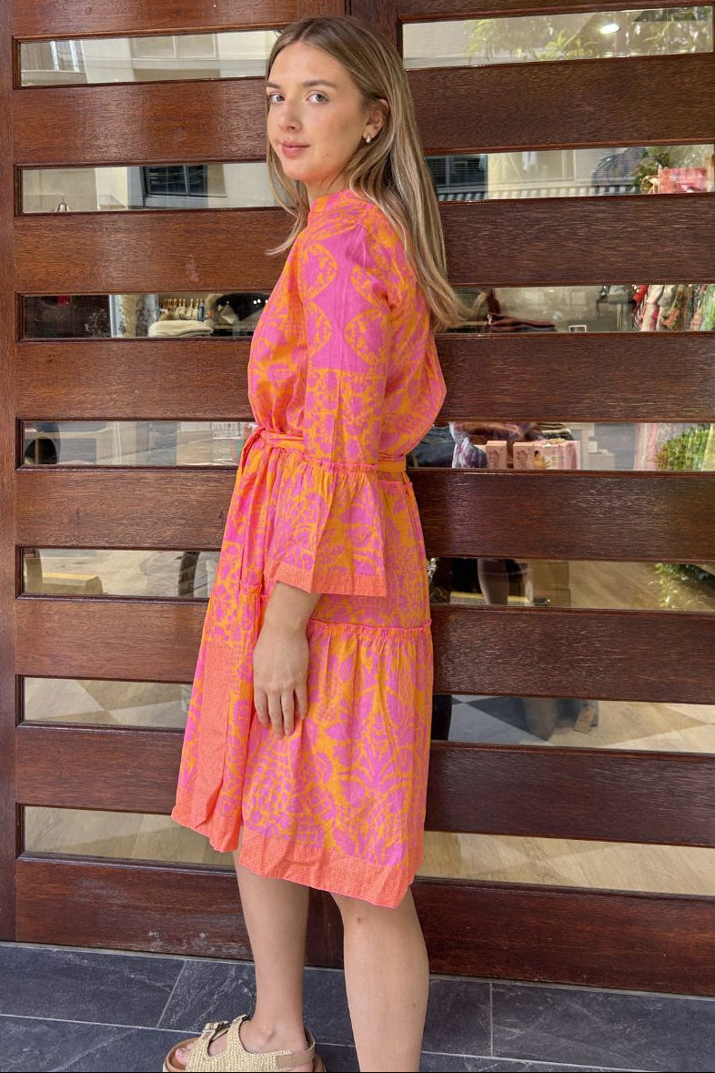 Woman in a pink and orange dress standing in front of a wooden gate.