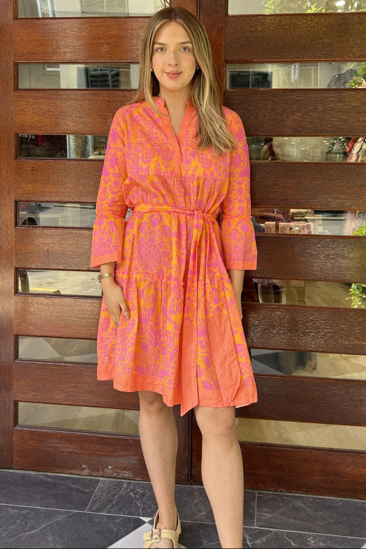 Woman wearing a pink dress with a pattern standing in front of a wooden gate.