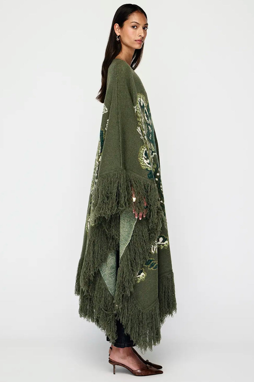 Woman wearing a long green embroidered kimono with fringe on a white background