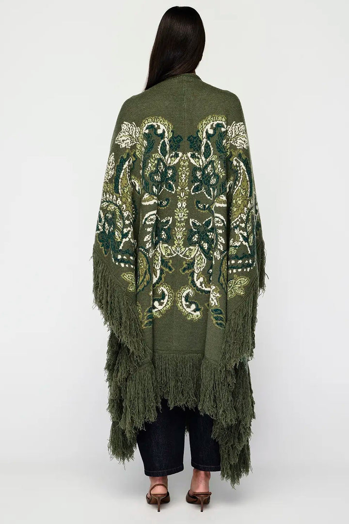 Person wearing a green embroidered poncho with fringe on a white background