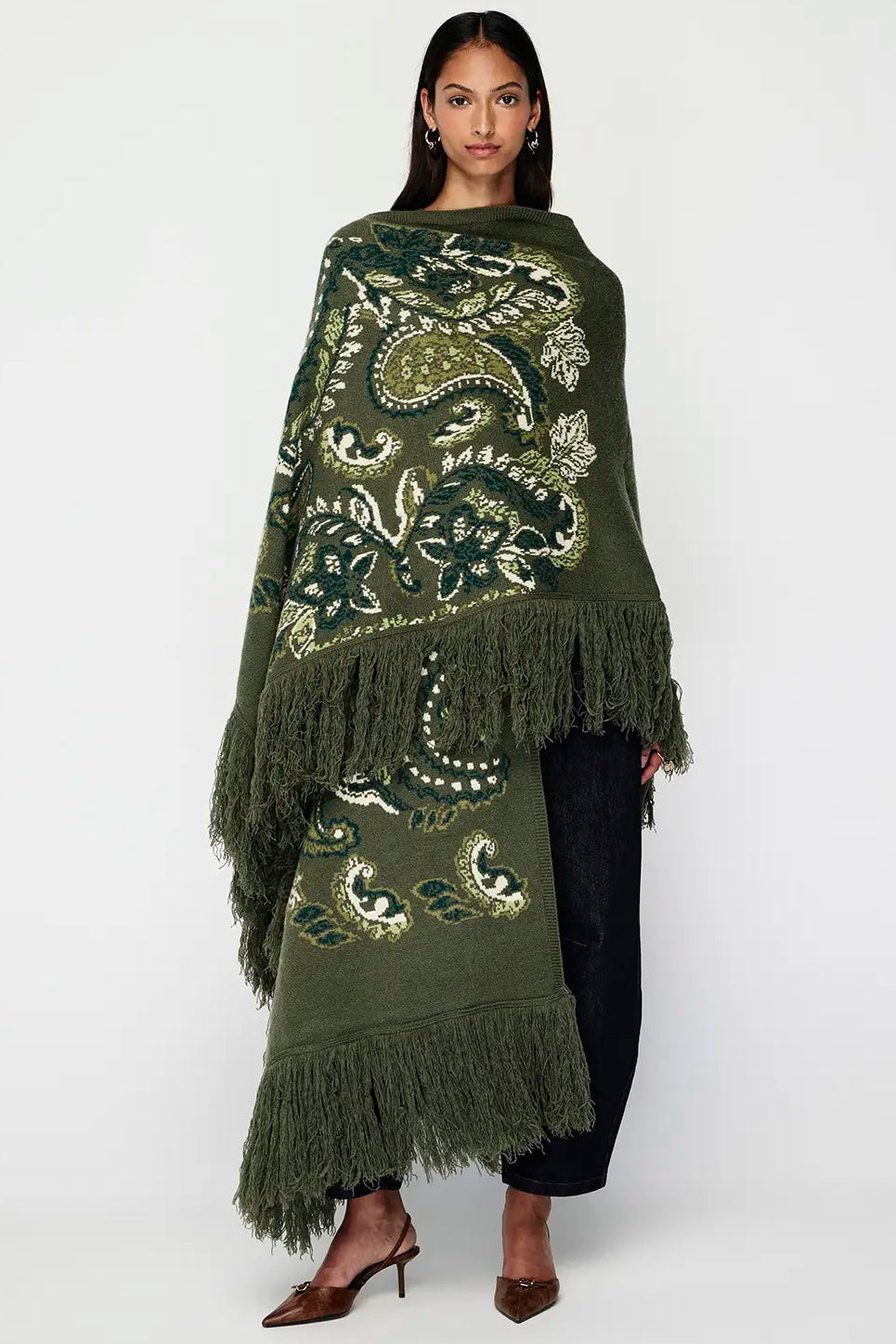 Woman wearing a green embroidered poncho with fringe on a white background