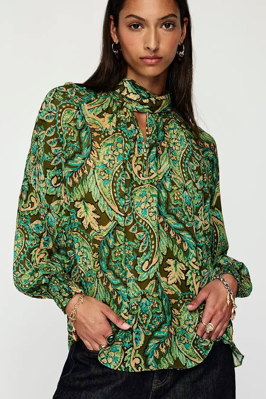 Woman wearing a green patterned blouse and black pants on a white background