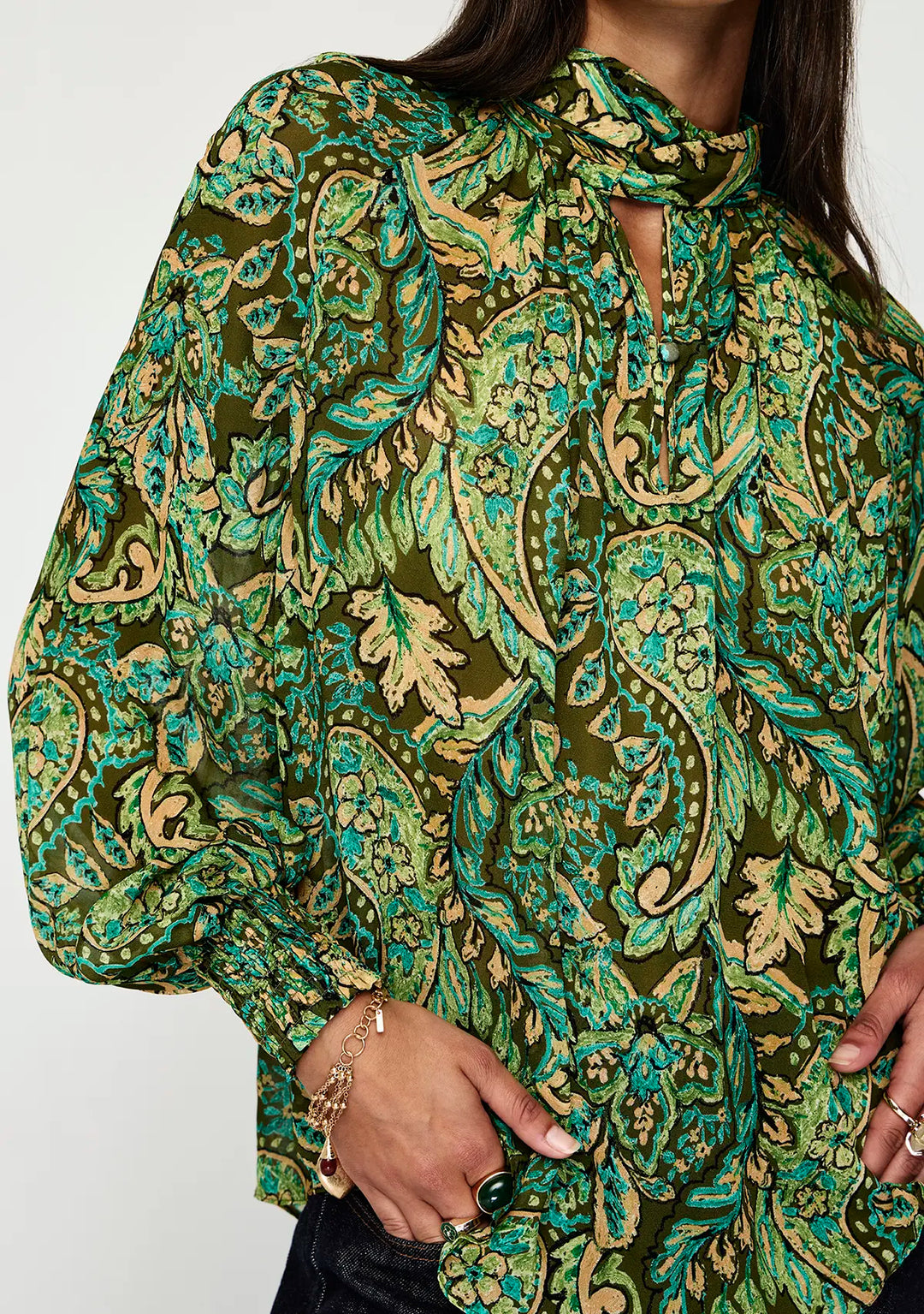 Green and gold patterned blouse worn by a person on a white background