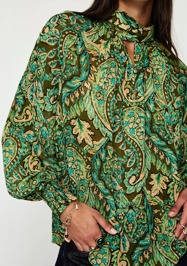 Green and gold patterned blouse worn by a person on a white background
