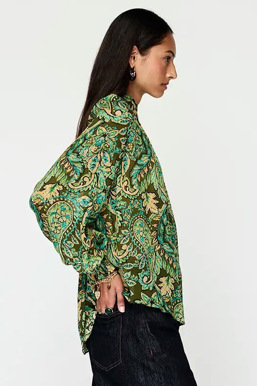 Woman wearing a green patterned blouse and black pants on a white background