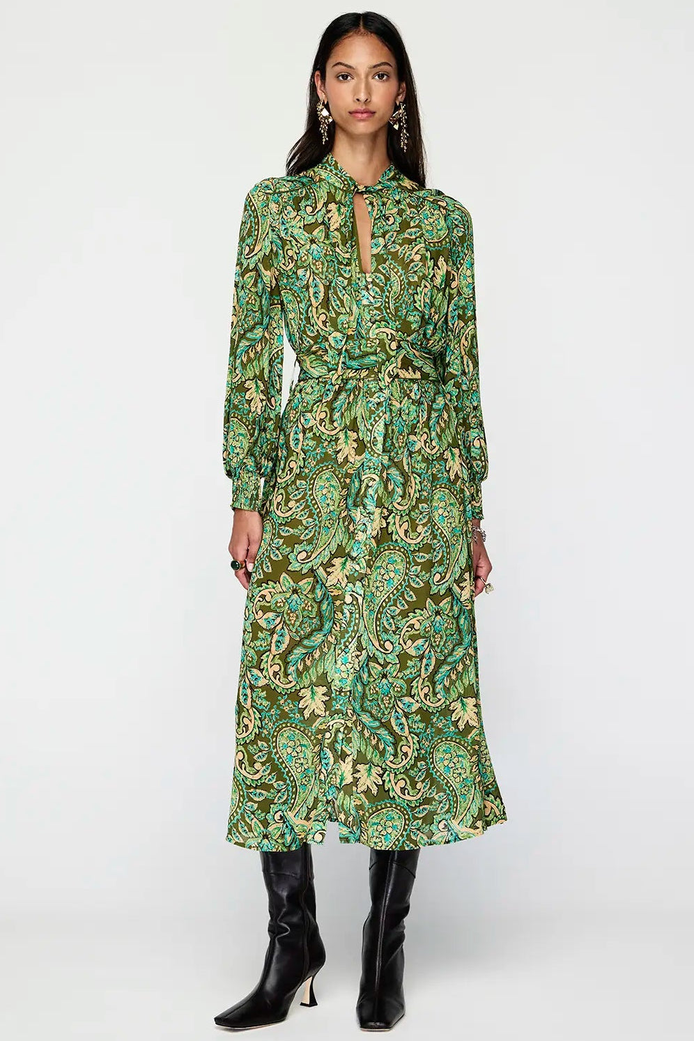 Woman wearing a green patterned dress with black boots on a white background