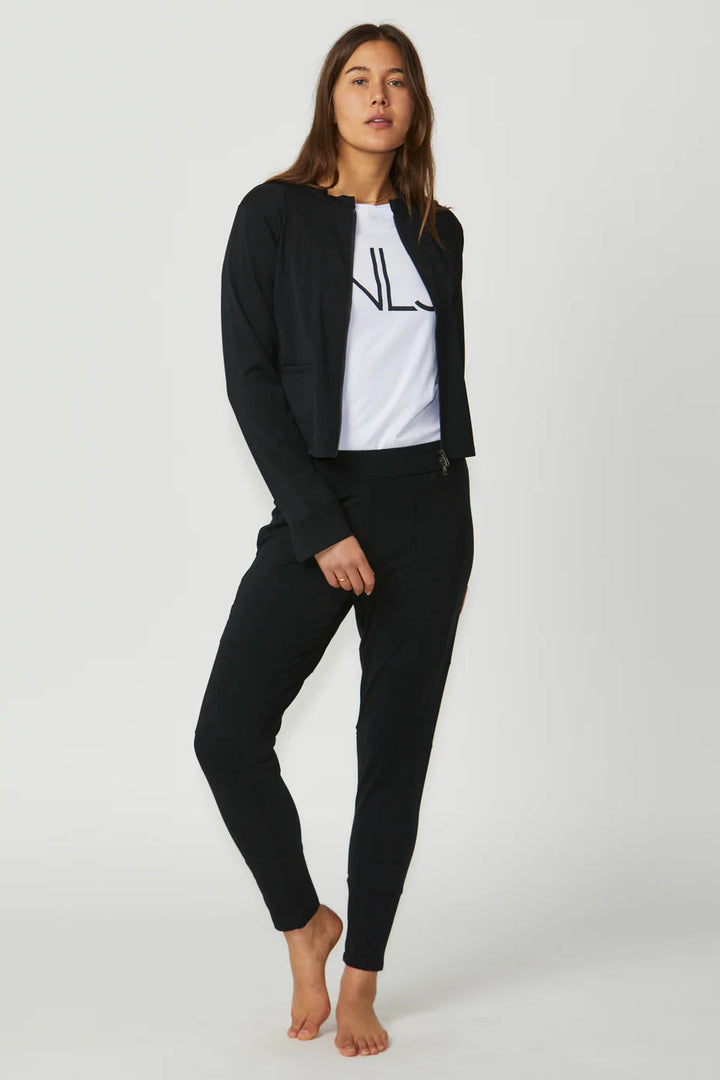 Woman wearing a black jacket, white shirt with logo, and black pants on a white background