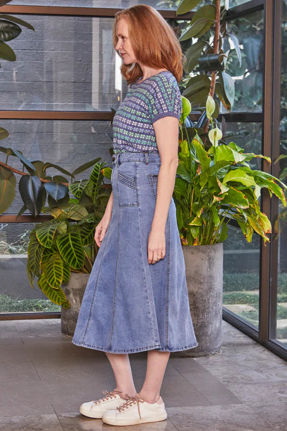 Woman in a blue dress standing in a modern indoor setting with plants.