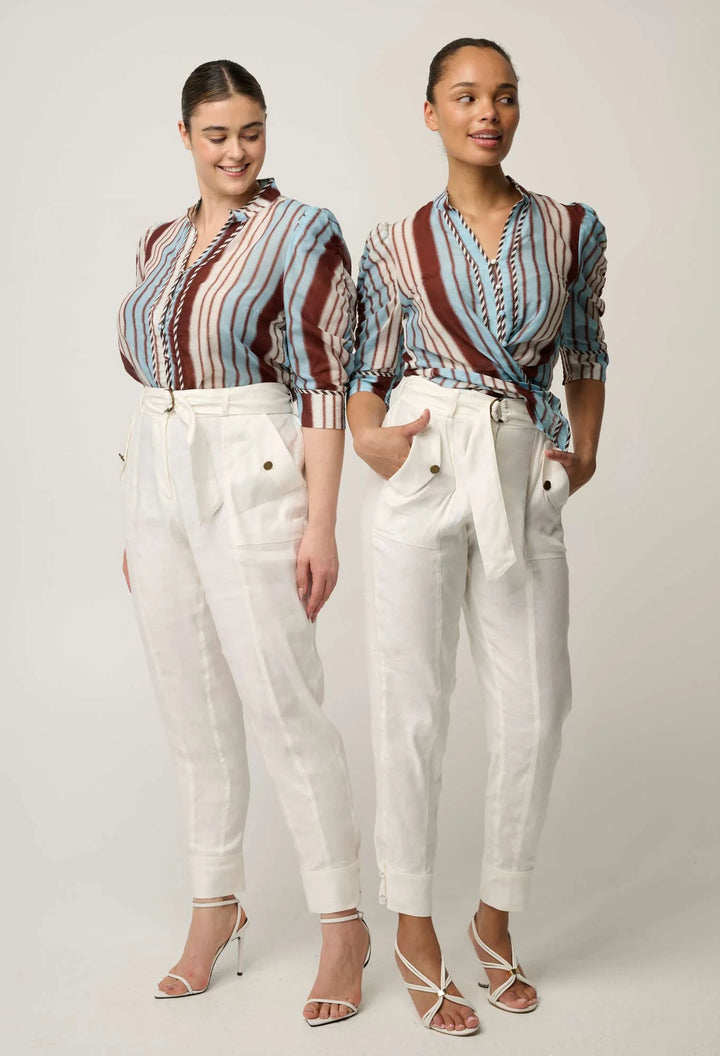 Two models wearing matching outfits consisting of a striped and patterned wrap-style blouse with white trousers, standing against a light gray studio background.