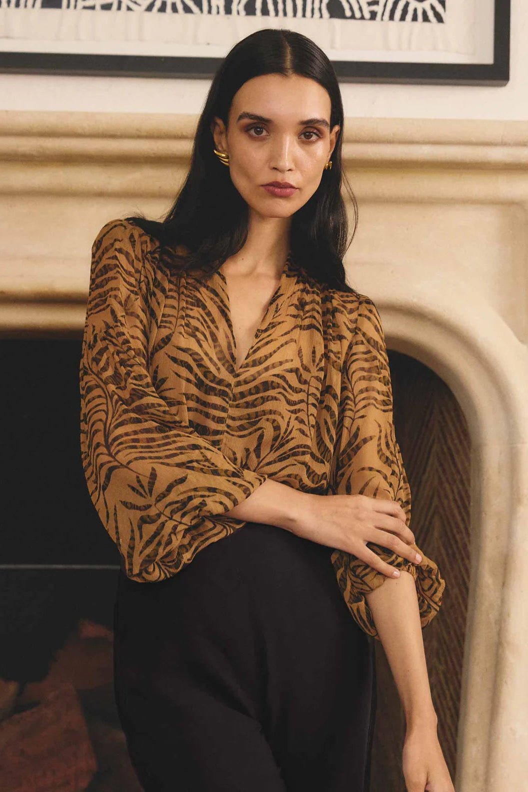 Woman wearing a patterned top in front of a fireplace