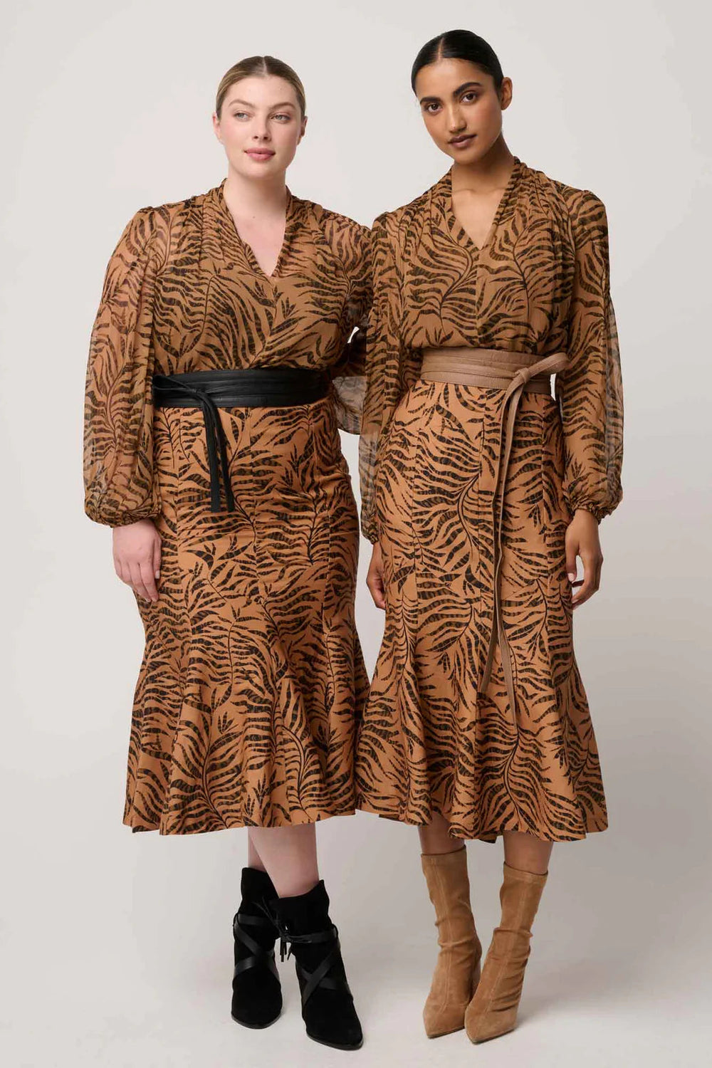 Two women wearing tiger print dresses on a plain background