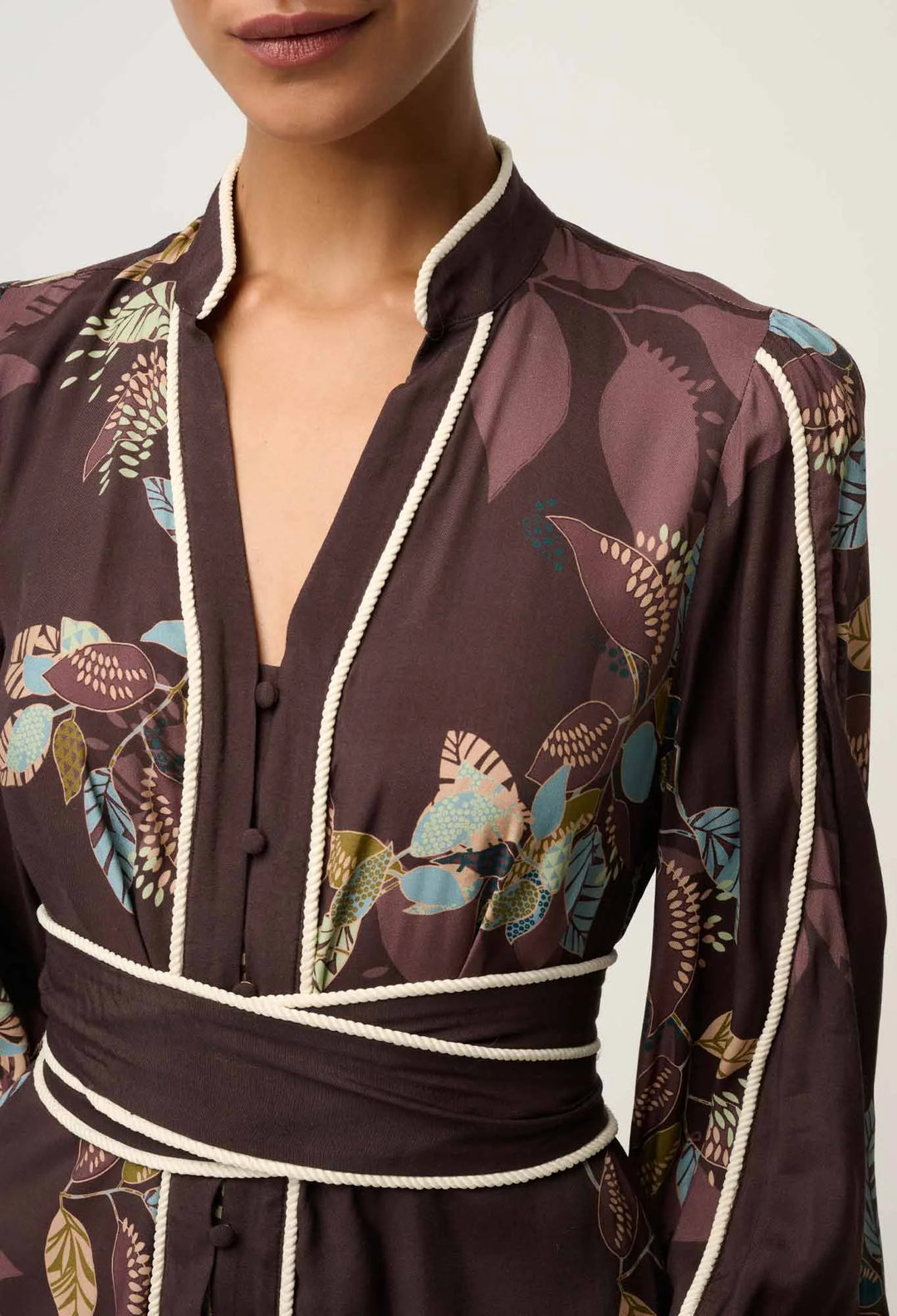 Woman wearing a dark brown floral patterned outfit with white trim on a neutral background