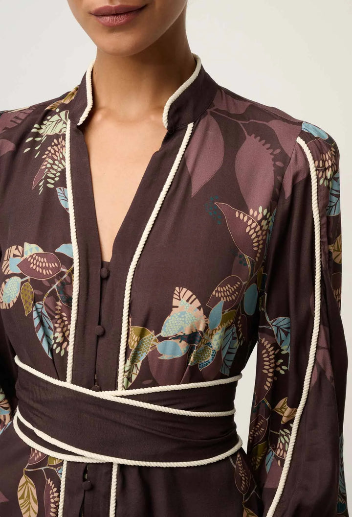 Woman wearing a dark brown floral patterned outfit with white trim on a neutral background