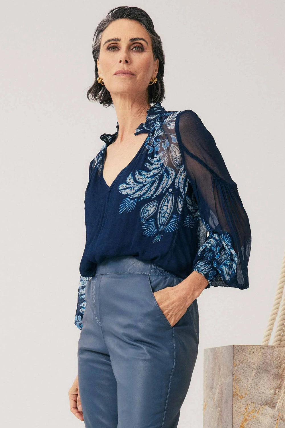 Woman wearing a dark blue embroidered blouse with sheer sleeves against a light background