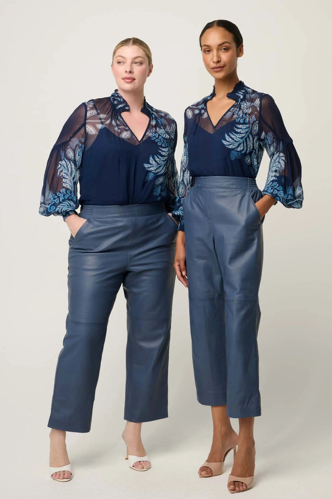 Two women wearing matching outfits with floral tops and blue pants on a white background