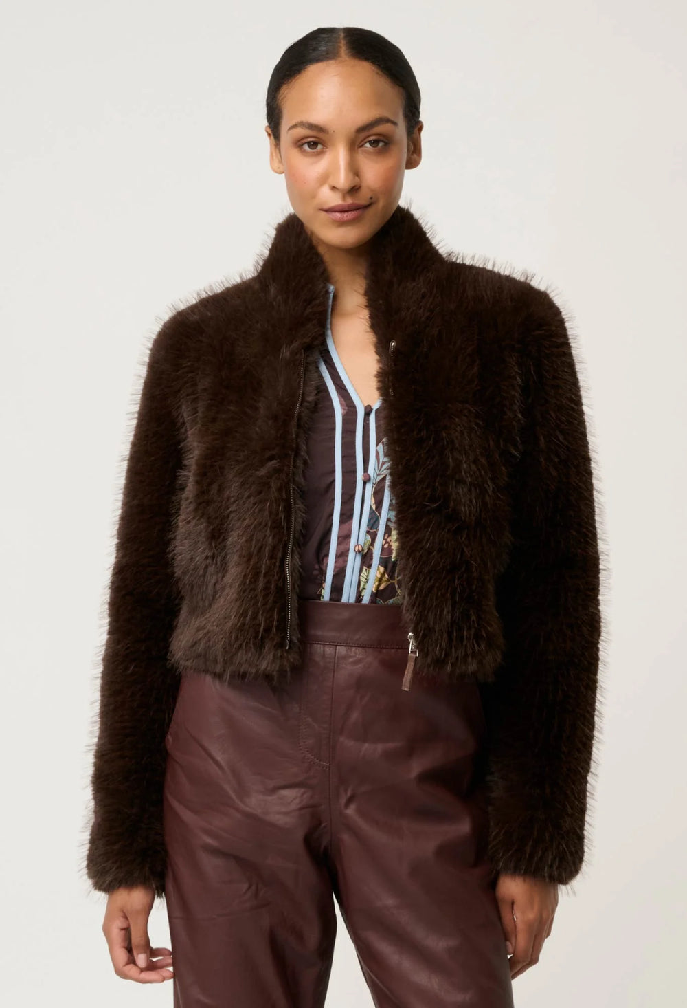 Woman wearing a brown fuzzy jacket and leather pants on a white background
