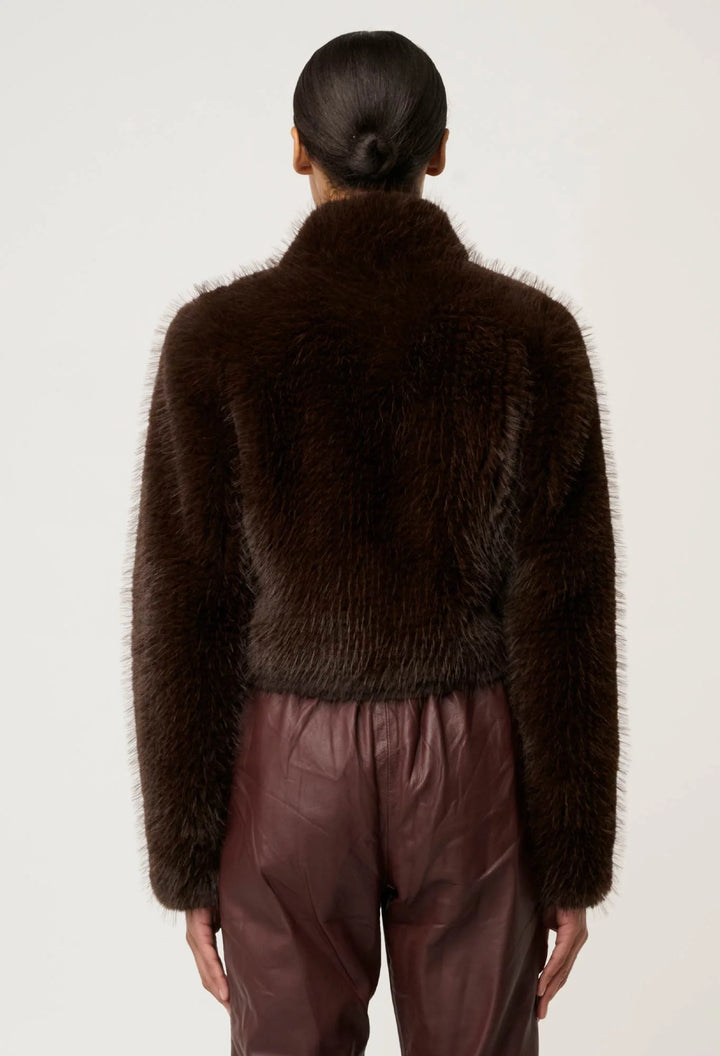 Person wearing a dark brown fuzzy sweater and brown pants on a white background