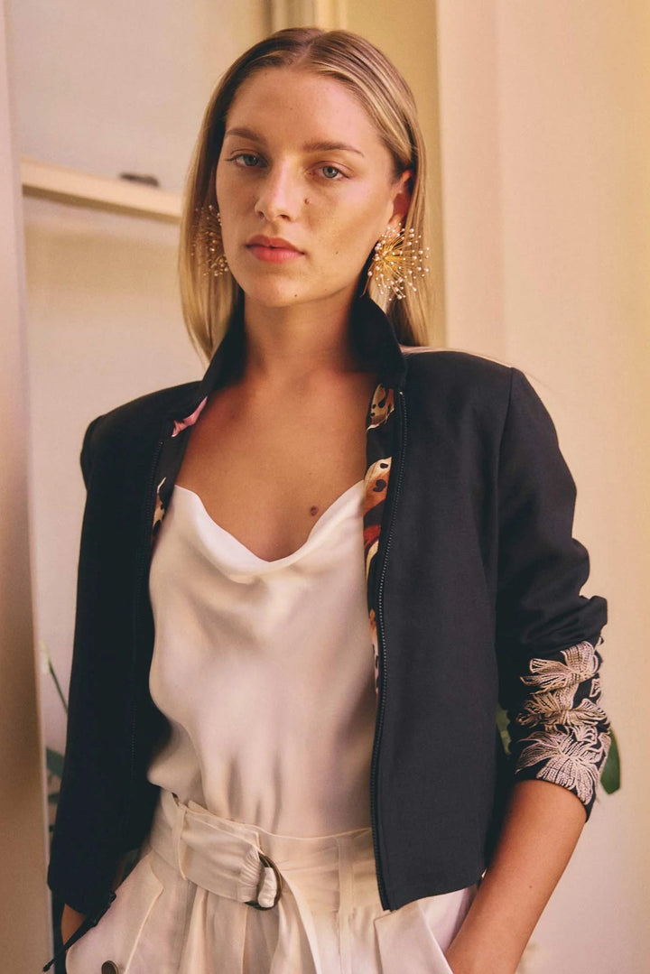Woman wearing a black blazer with floral cuffs and a white top, standing indoors.