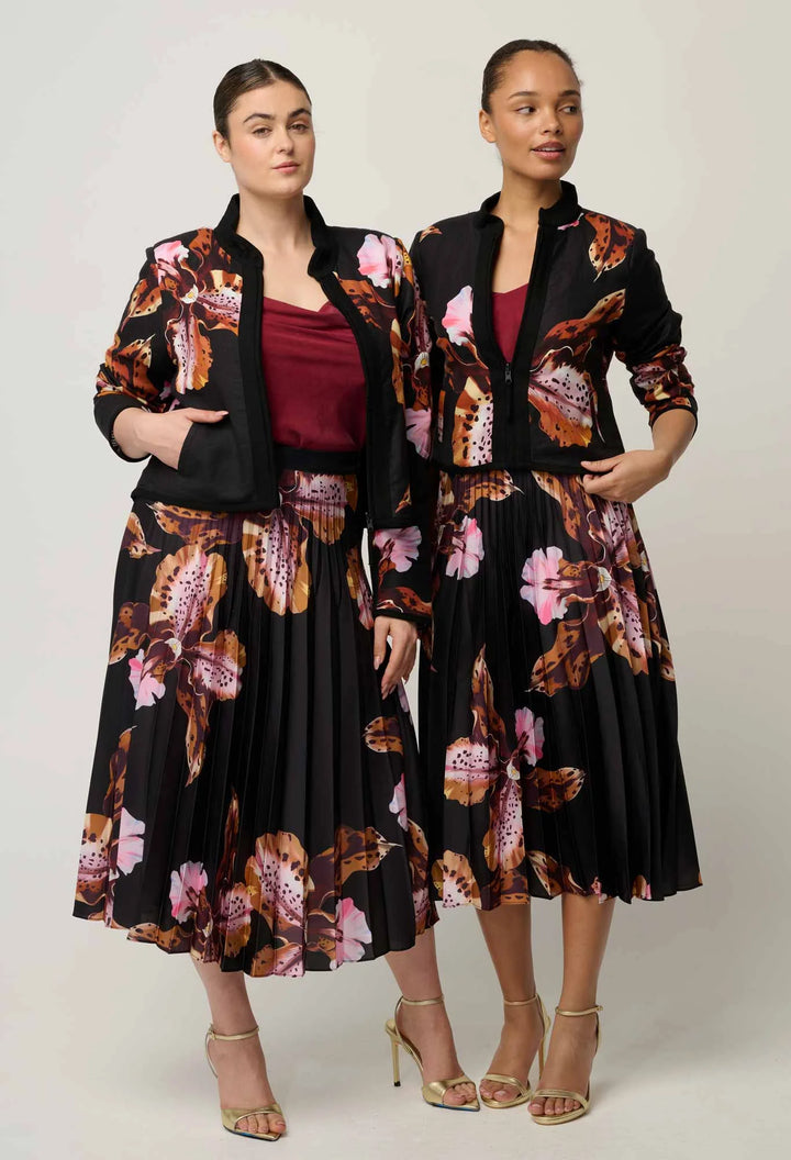 Two women modeling matching black midi skirts and blazers with a pink, brown, and gold floral print, styled with burgundy tops and gold heels against a light gray studio background.