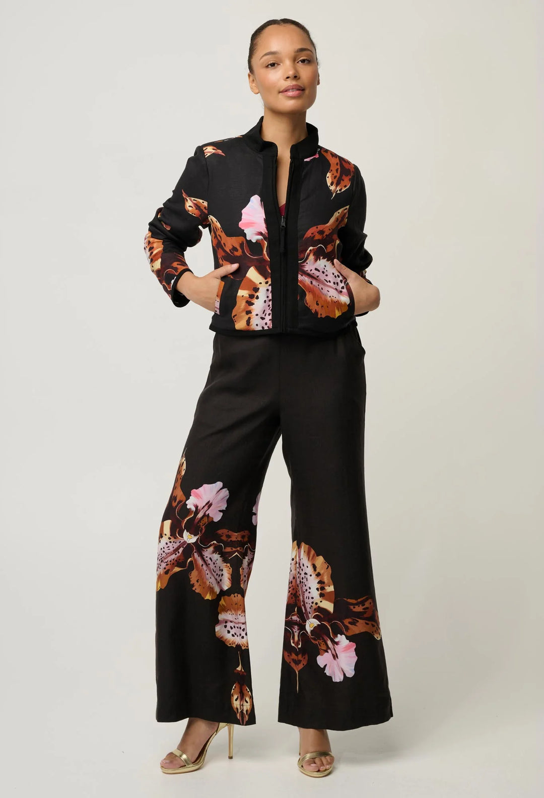 A model wearing a black two-piece jumpsuit with a colorful butterfly and floral print, standing against a light gray studio background.