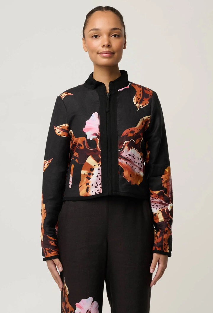 A model wearing a black cropped zip-up jacket with a colorful ice cream cone and dessert print on the front and sleeves, paired with black pants, against a light gray studio background.
