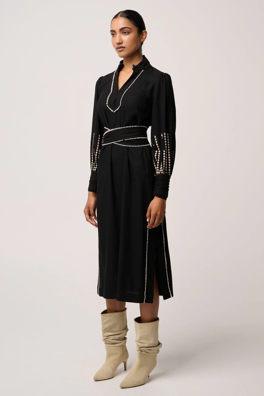 Woman wearing a black dress with decorative elements and beige boots on a white background