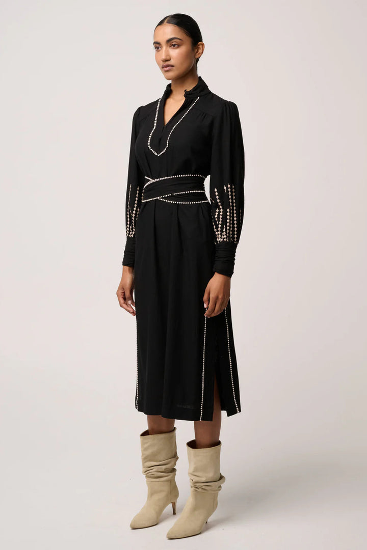 Woman wearing a black dress with decorative elements and beige boots on a white background
