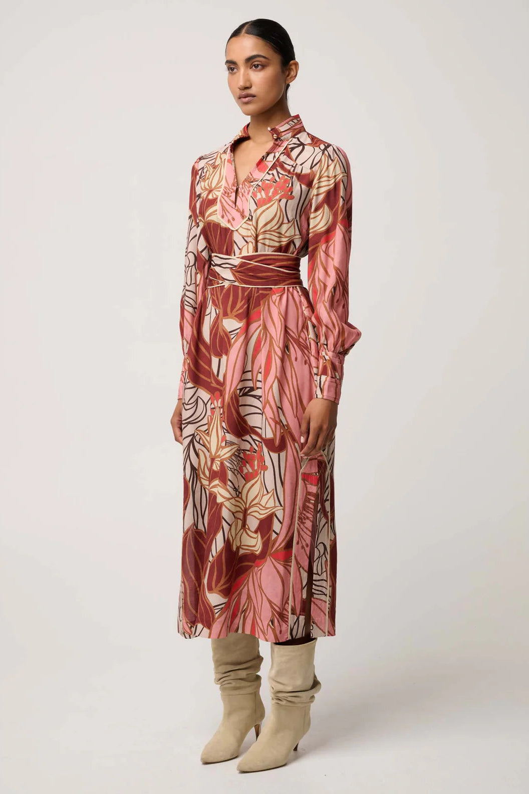 Woman wearing a long, patterned dress with beige boots on a white background