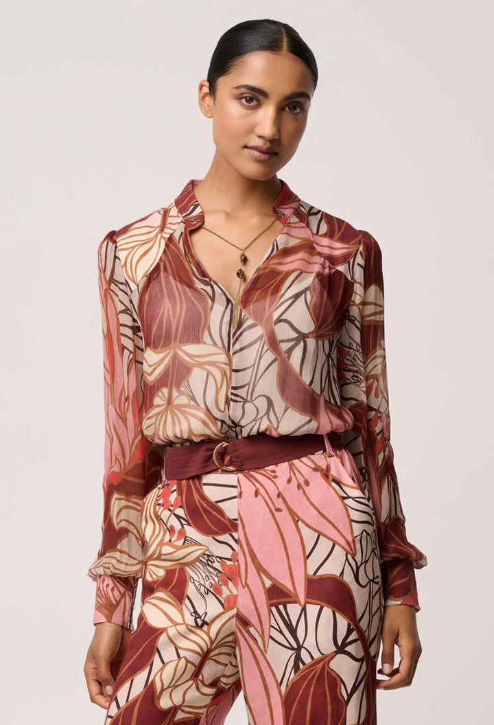Woman wearing a patterned outfit with a belt on a plain background