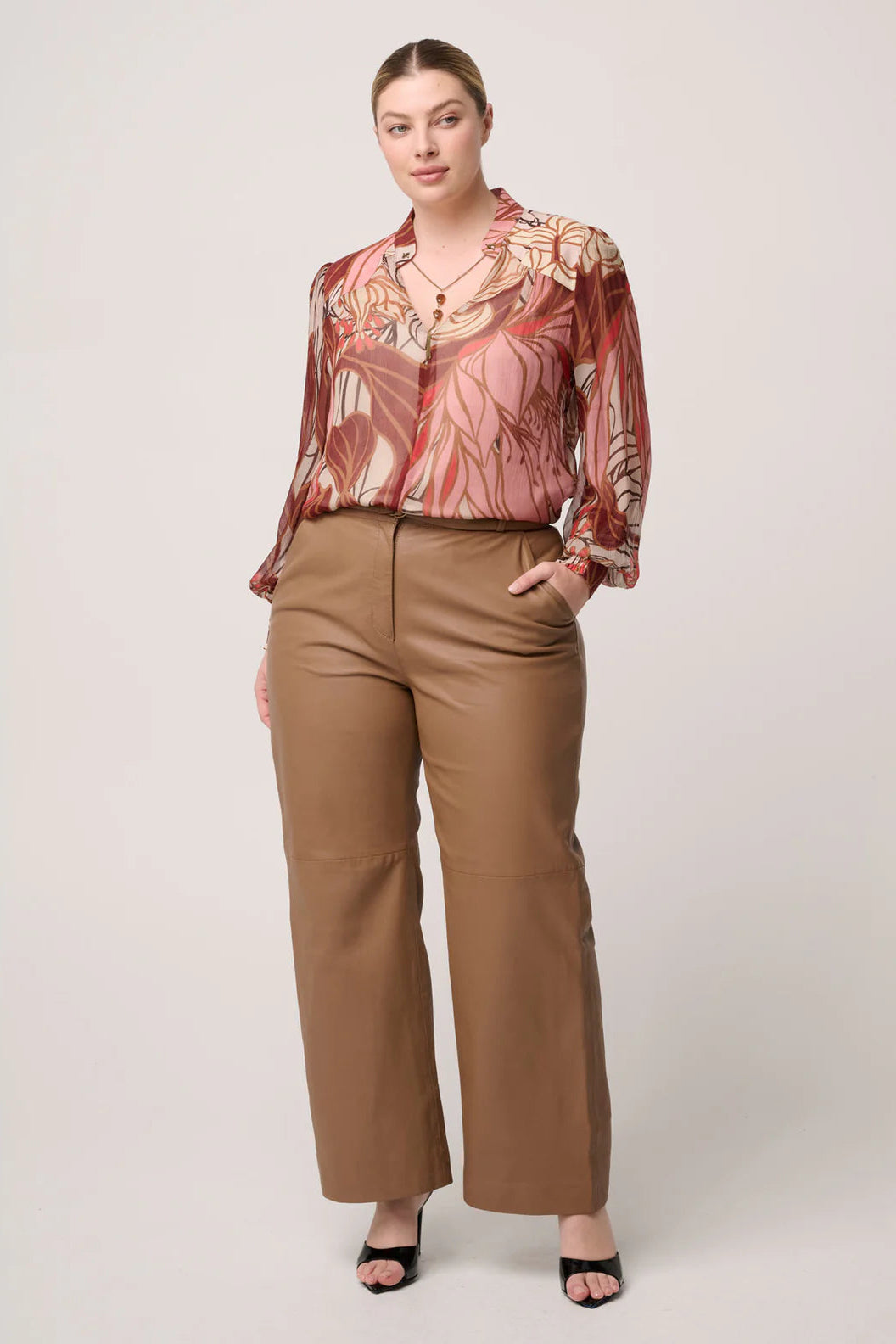 Woman wearing a patterned blouse and brown pants on a white background