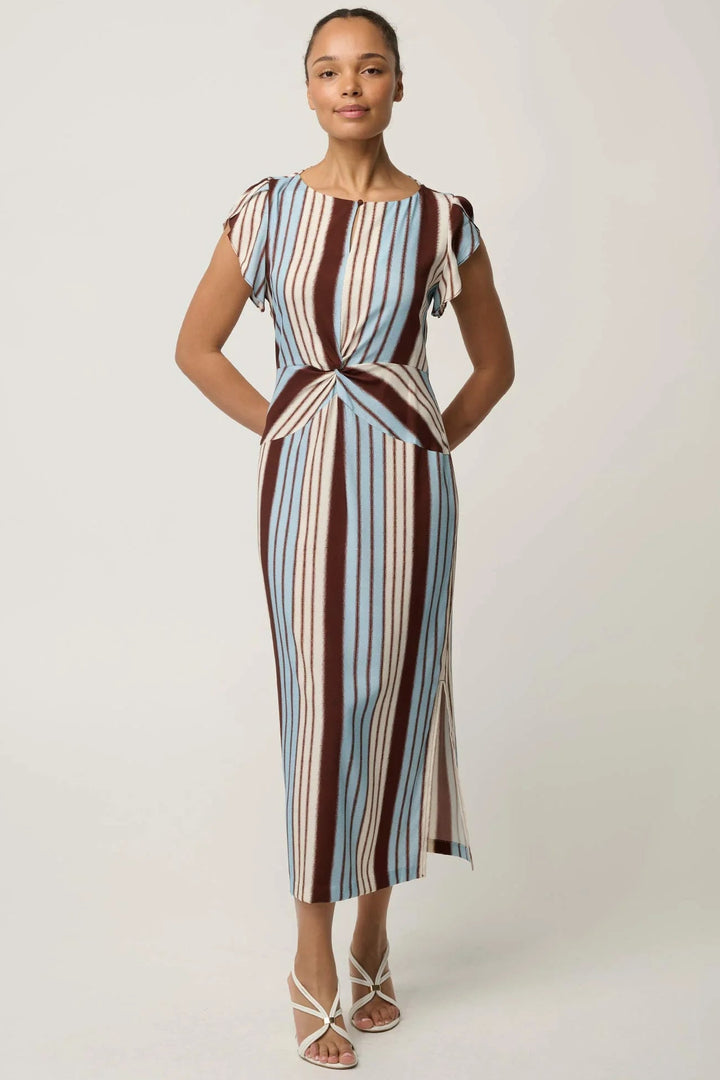 A woman modeling a midi-length dress with vertical stripes in brown, light blue, cream, and white, featuring cap sleeves and a twisted waist detail, set against a plain light gray studio background.