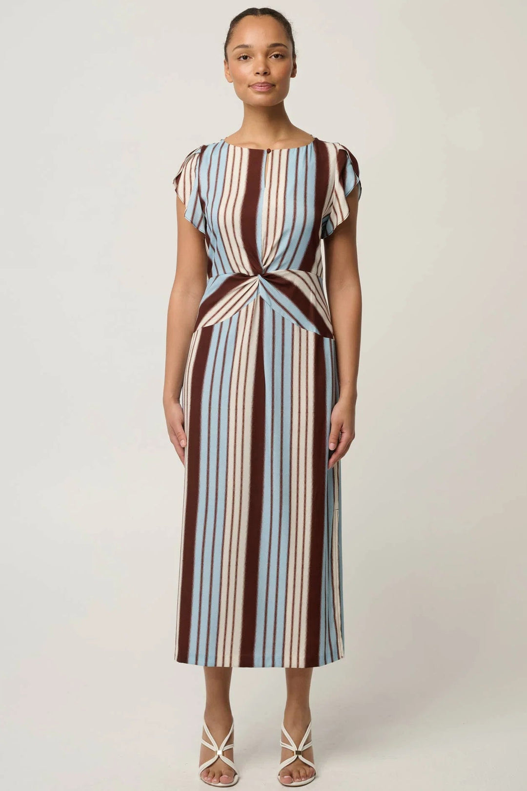 A woman modeling a midi dress with vertical stripes in brown, cream, and light blue, featuring cap sleeves and a twisted waist detail, set against a plain light gray background.