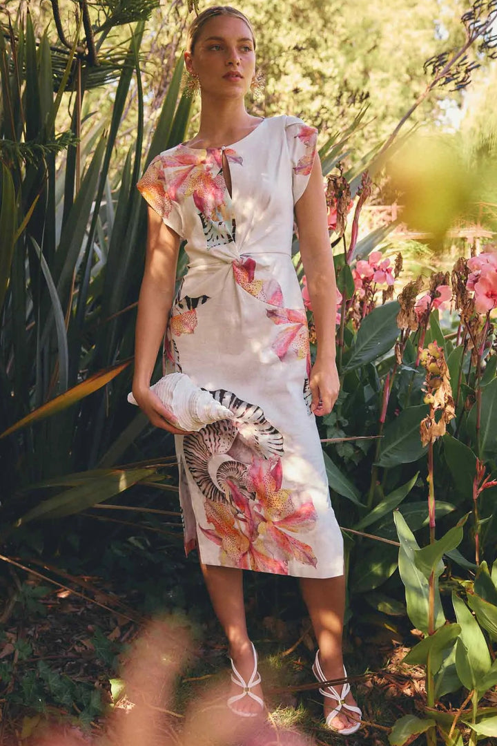 Woman in a floral dress standing in a garden with greenery and flowers.