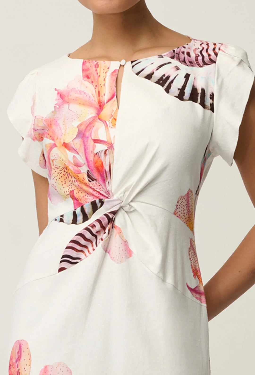 A close-up of a woman wearing a white dress with a colorful tropical floral and zebra print, featuring a keyhole neckline with a button and a twisted front detail.
